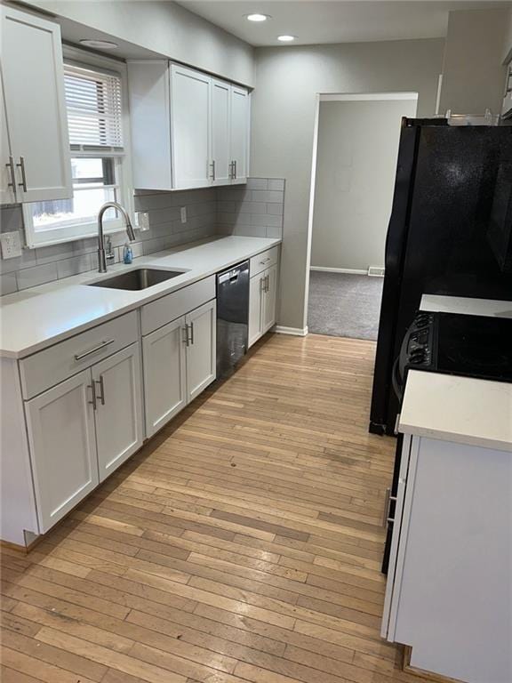 kitchen featuring sink, white cabinetry, light wood-type flooring, decorative backsplash, and black appliances