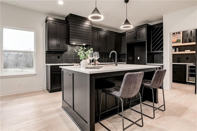 kitchen with sink, a kitchen island with sink, light hardwood / wood-style floors, decorative light fixtures, and decorative backsplash