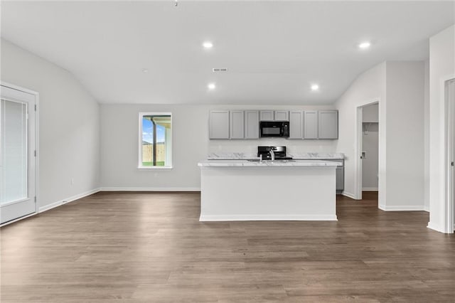 kitchen featuring stainless steel stove, hardwood / wood-style floors, lofted ceiling, a kitchen island with sink, and gray cabinets