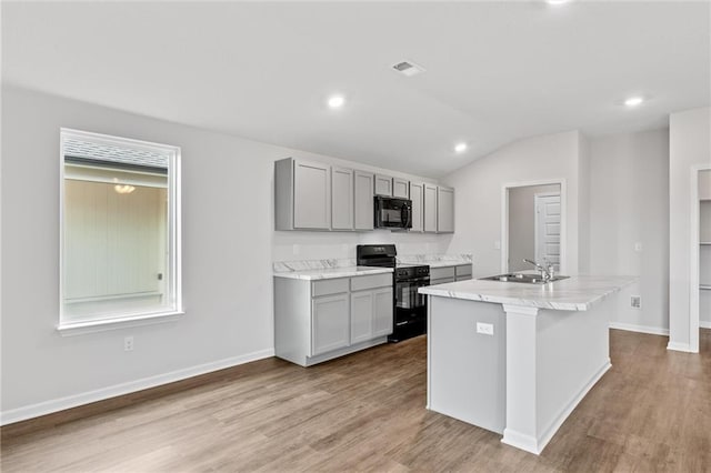 kitchen featuring vaulted ceiling, an island with sink, black appliances, gray cabinetry, and sink