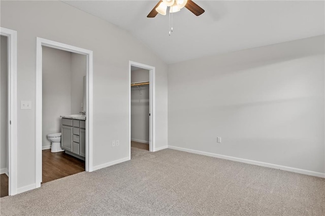 unfurnished bedroom featuring lofted ceiling, ceiling fan, dark colored carpet, a walk in closet, and ensuite bath