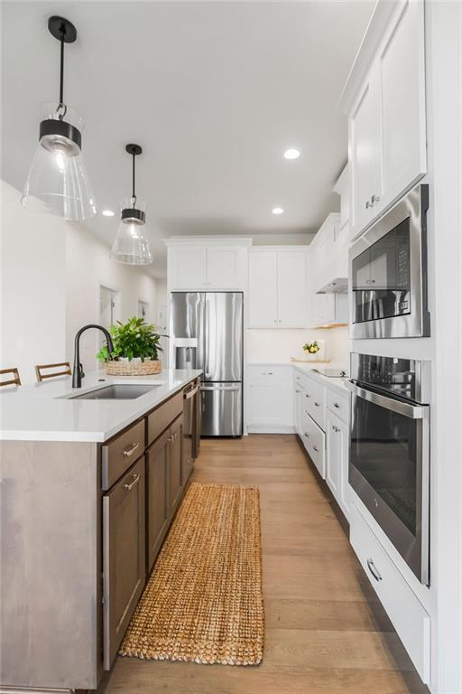 4102 W 158th Ter, Overland Park, KS 66224 - kitchen featuring appliances with stainless steel finishes, a sink, light countertops, a center island with sink, and light wood-style flooring