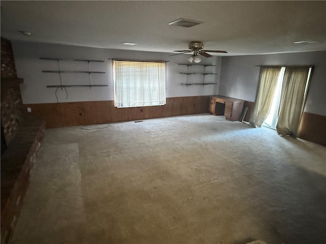 unfurnished living room with carpet flooring, wood walls, and ceiling fan