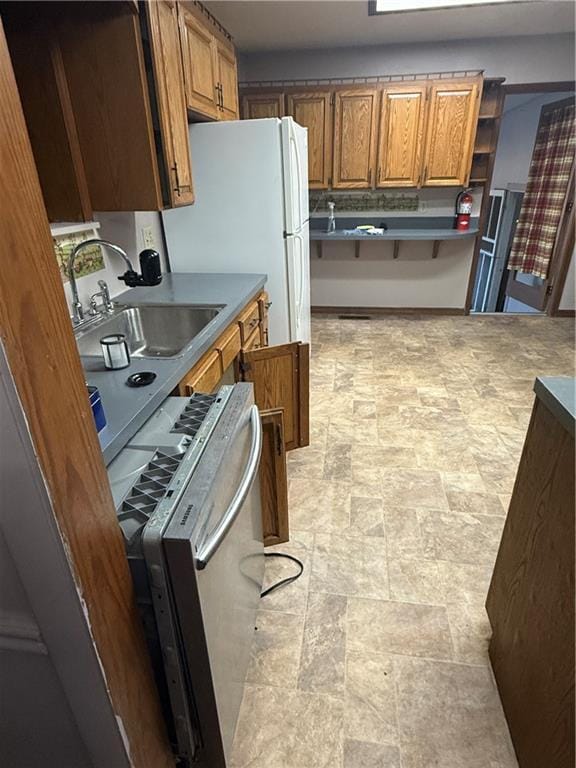 2123 N 8th St, Independence, KS 67301 - kitchen featuring brown cabinets, stone finish flooring, and freestanding refrigerator