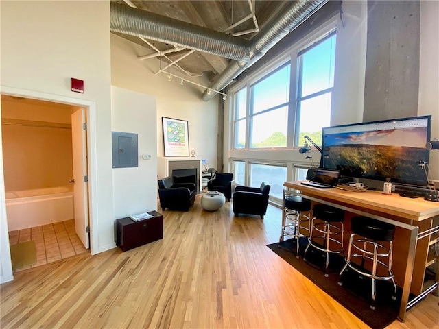 home office with a towering ceiling, light wood-type flooring, and electric panel