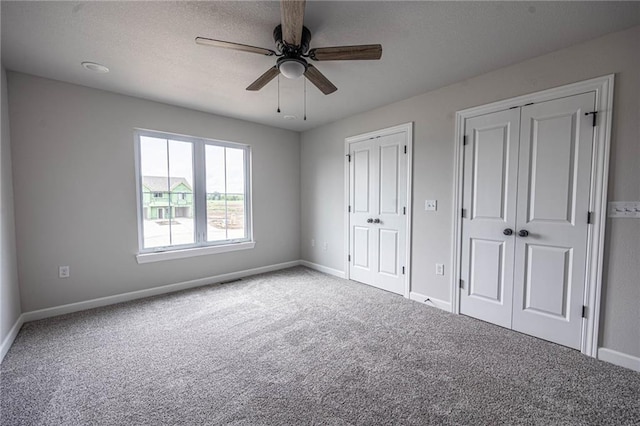 unfurnished bedroom featuring carpet flooring, a textured ceiling, ceiling fan, and multiple closets