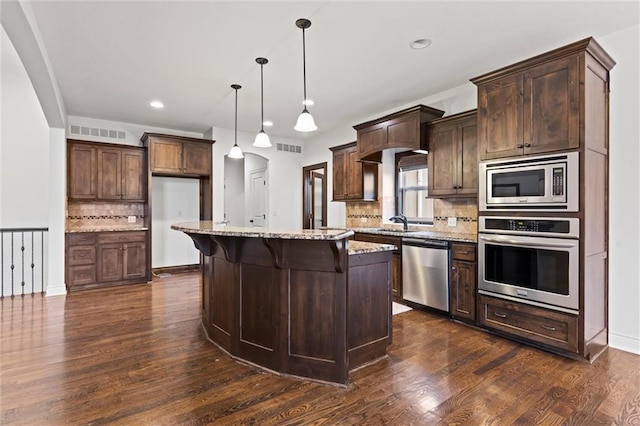 kitchen with dark hardwood / wood-style flooring, light stone counters, stainless steel appliances, decorative light fixtures, and a kitchen island