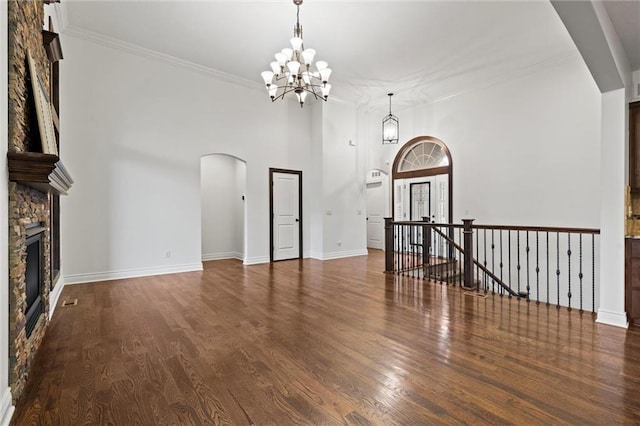 unfurnished living room featuring a towering ceiling, crown molding, a fireplace, a chandelier, and dark hardwood / wood-style floors