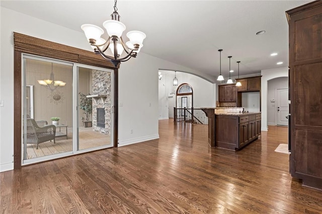 kitchen with a stone fireplace, light stone counters, dark hardwood / wood-style flooring, a notable chandelier, and decorative light fixtures