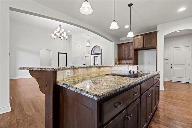 kitchen with pendant lighting, dark hardwood / wood-style floors, light stone countertops, and backsplash