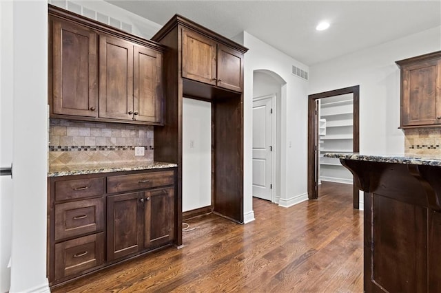 kitchen featuring dark brown cabinets, dark hardwood / wood-style flooring, light stone countertops, and backsplash