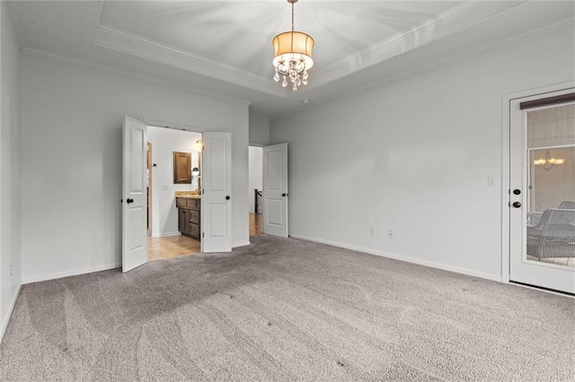 unfurnished bedroom featuring ensuite bath, ornamental molding, a tray ceiling, a notable chandelier, and light colored carpet