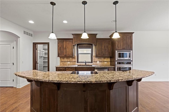 kitchen featuring pendant lighting, decorative backsplash, stainless steel appliances, and light hardwood / wood-style flooring