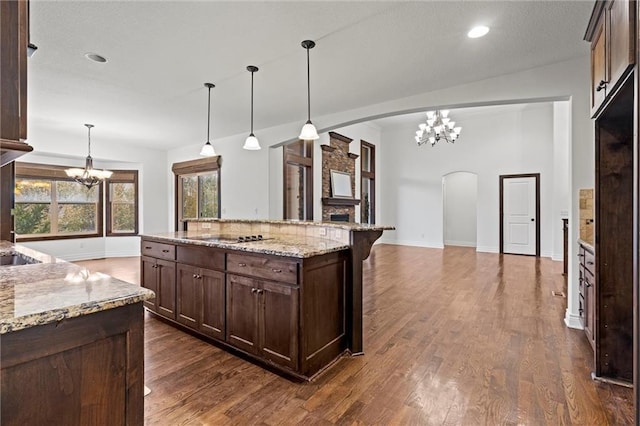 kitchen with light stone countertops, dark brown cabinets, hanging light fixtures, and lofted ceiling