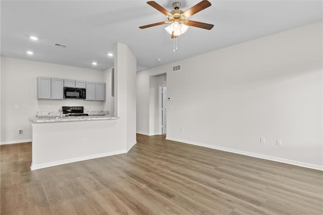 kitchen featuring light wood-type flooring, gray cabinets, light stone counters, and black appliances