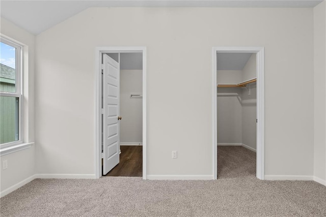 unfurnished bedroom featuring lofted ceiling, dark carpet, a walk in closet, and a closet