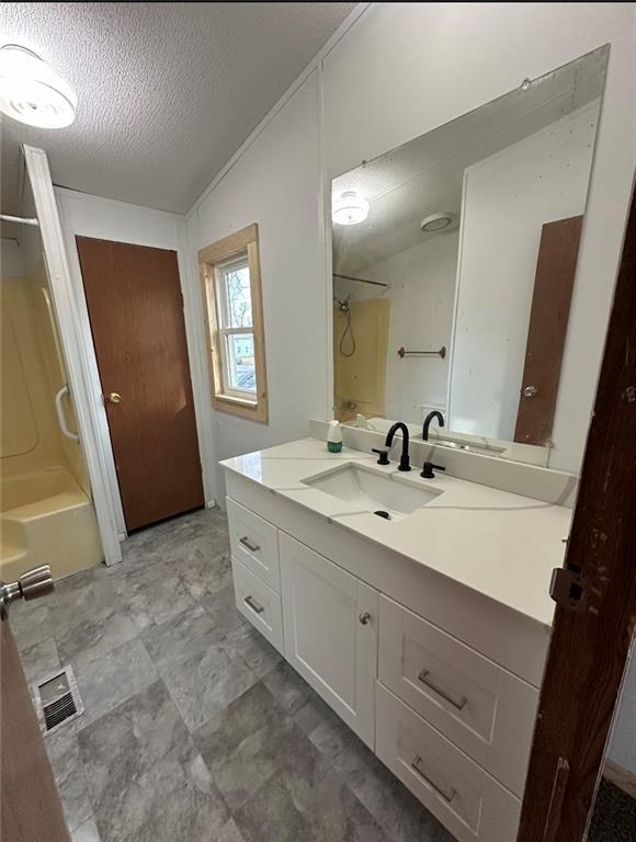 bathroom featuring shower / tub combination, vaulted ceiling, vanity, and a textured ceiling