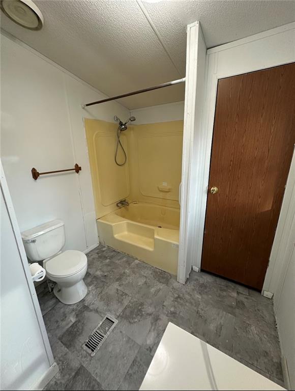 bathroom featuring washtub / shower combination, toilet, and a textured ceiling