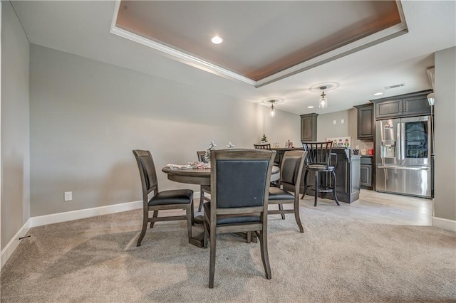 dining area with a raised ceiling, ornamental molding, and light carpet