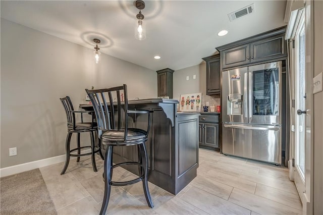 kitchen featuring stainless steel fridge, dark brown cabinetry, a breakfast bar area, and backsplash