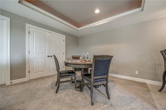 carpeted dining space with a tray ceiling and crown molding