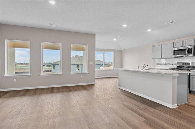 kitchen with sink, tasteful backsplash, gray cabinets, a kitchen island with sink, and appliances with stainless steel finishes