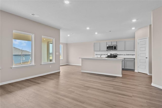 kitchen featuring gray cabinetry, a kitchen island with sink, sink, appliances with stainless steel finishes, and light hardwood / wood-style floors