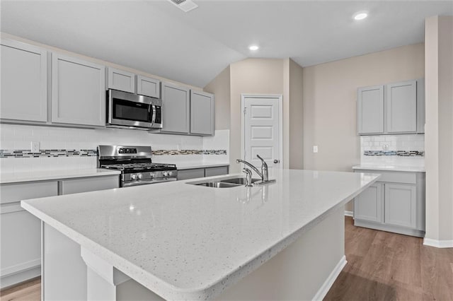 kitchen with sink, stainless steel appliances, backsplash, lofted ceiling, and a kitchen island with sink