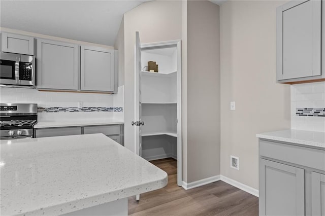 kitchen with decorative backsplash, light stone counters, stainless steel appliances, and light hardwood / wood-style flooring