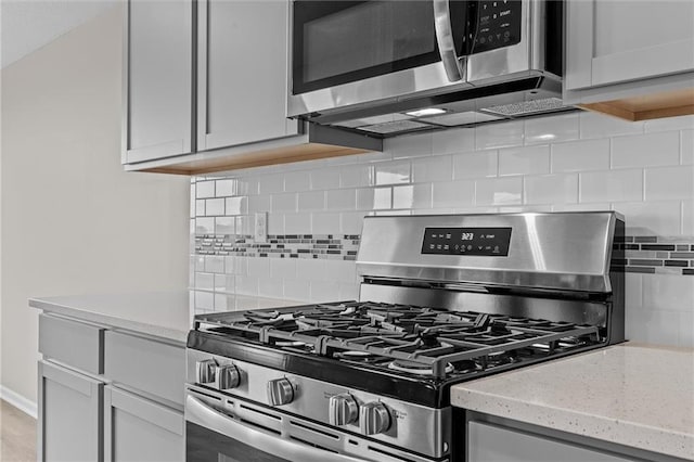 kitchen featuring backsplash, light stone countertops, light hardwood / wood-style floors, and appliances with stainless steel finishes