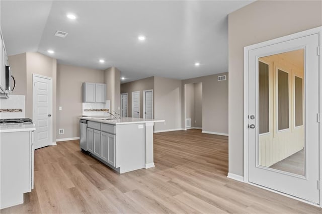 kitchen featuring gray cabinetry, backsplash, sink, stainless steel dishwasher, and an island with sink