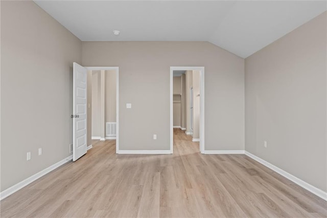 unfurnished bedroom featuring vaulted ceiling, light hardwood / wood-style floors, a spacious closet, and a closet