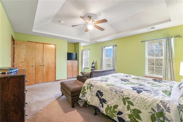 bedroom with a tray ceiling, ceiling fan, light carpet, and a textured ceiling