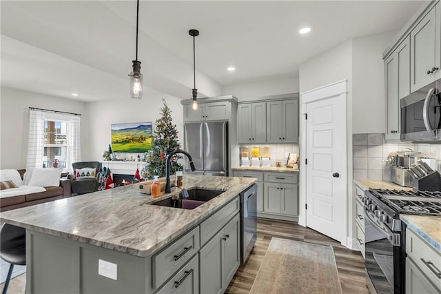 kitchen with backsplash, gray cabinetry, stainless steel appliances, a kitchen island with sink, and sink