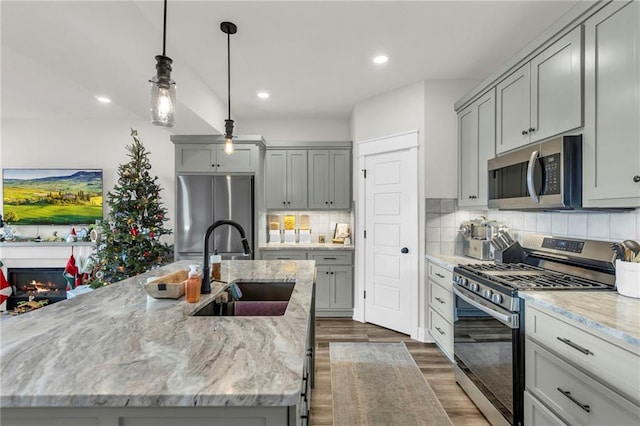 kitchen featuring backsplash, stainless steel appliances, sink, a center island with sink, and gray cabinets