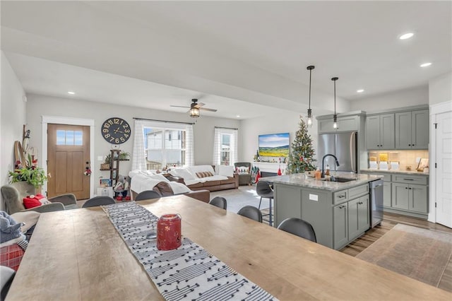 kitchen with a center island with sink, sink, hanging light fixtures, gray cabinets, and stainless steel appliances