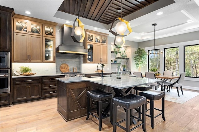 21359 W 93rd Ct, Lenexa, KS 66220 - kitchen with a sink, wall chimney range hood, a tray ceiling, appliances with stainless steel finishes, and light wood finished floors