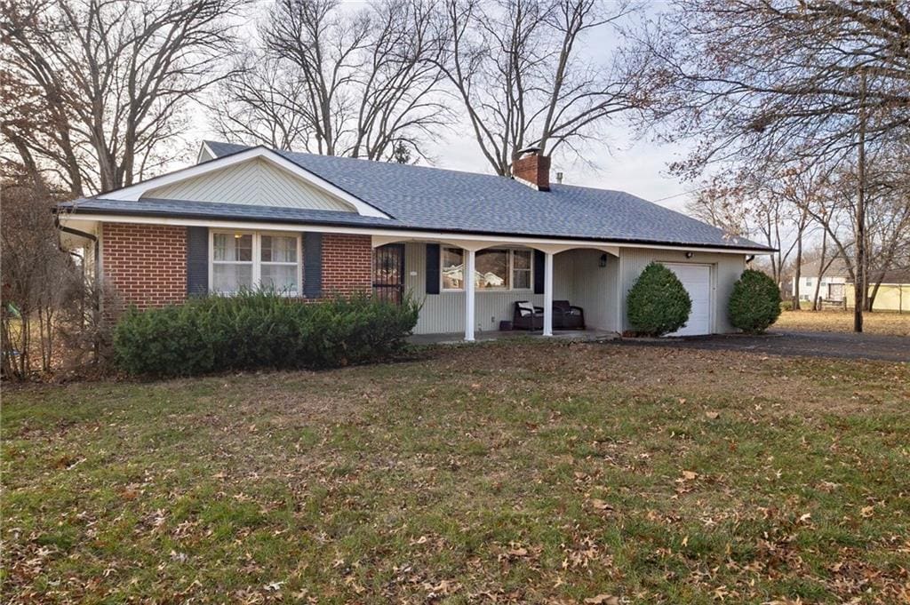 ranch-style house featuring covered porch, a front yard, and a garage