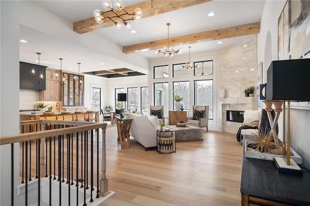 living room with a chandelier, light hardwood / wood-style floors, beam ceiling, and a tile fireplace