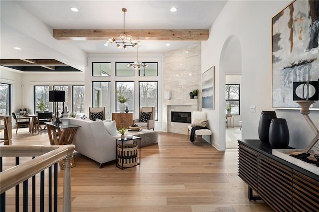 living room with beam ceiling, light wood-type flooring, a notable chandelier, and a fireplace