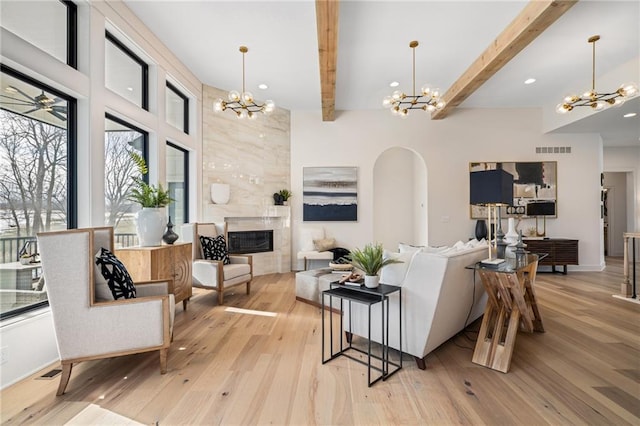 living room featuring ceiling fan with notable chandelier, light hardwood / wood-style flooring, beam ceiling, and a fireplace