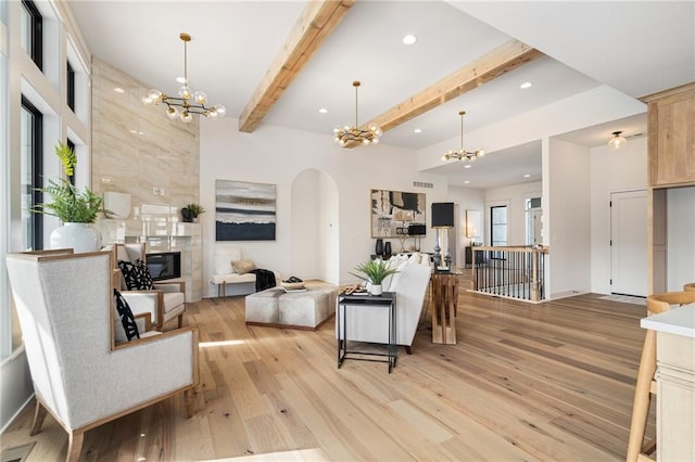 living room featuring beam ceiling, a notable chandelier, a fireplace, and light hardwood / wood-style floors