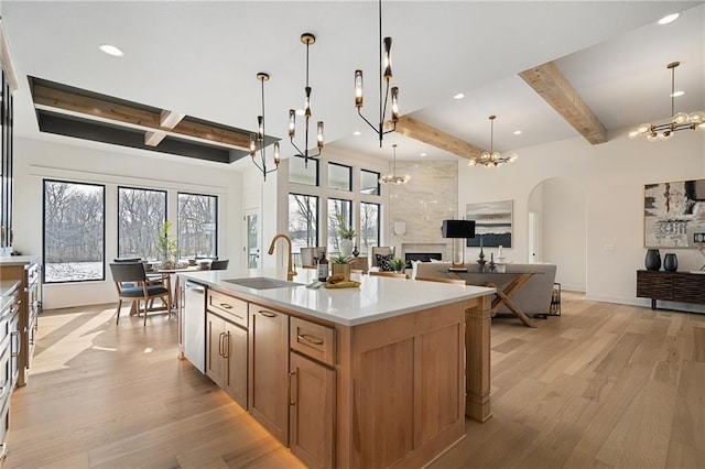 kitchen with a center island with sink, stainless steel dishwasher, sink, beamed ceiling, and an inviting chandelier