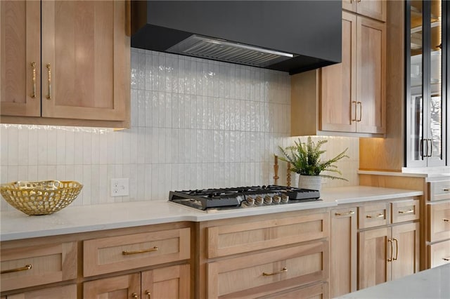 kitchen with stainless steel gas cooktop, light brown cabinetry, backsplash, and wall chimney range hood