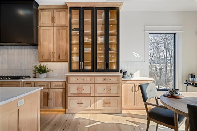 bar with light hardwood / wood-style floors, backsplash, stainless steel gas cooktop, and wall chimney exhaust hood