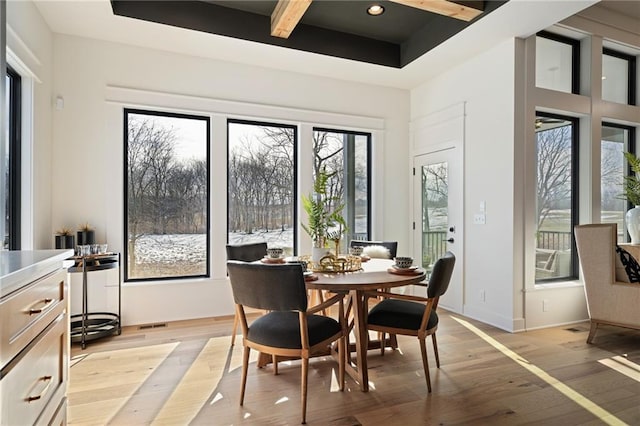 dining area featuring light wood-type flooring, beam ceiling, and a tray ceiling