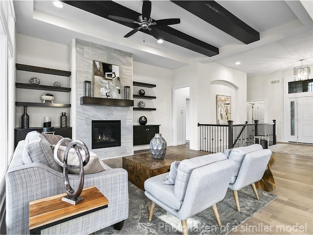 living room with built in shelves, ceiling fan, wood-type flooring, beam ceiling, and a fireplace