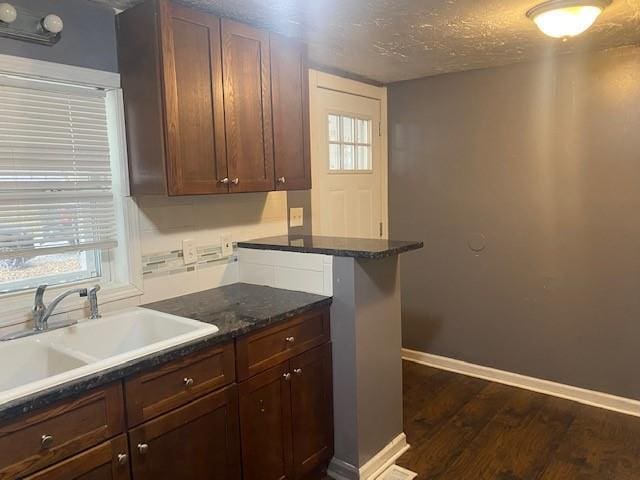 kitchen featuring kitchen peninsula, a textured ceiling, dark wood-type flooring, sink, and dark stone countertops