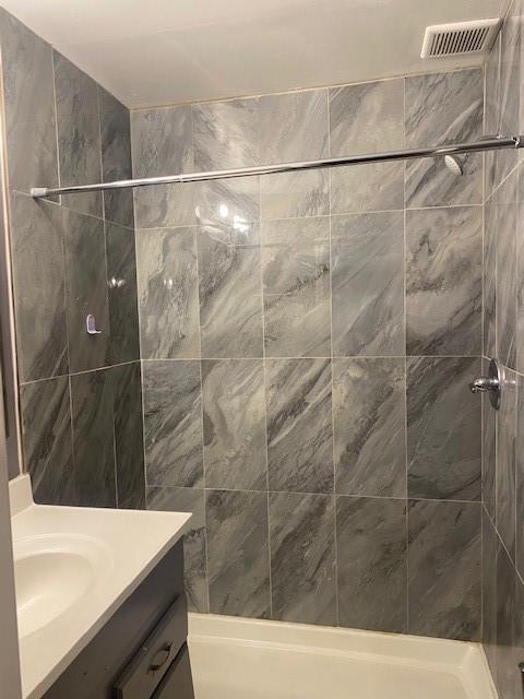 bathroom with a tile shower and vanity