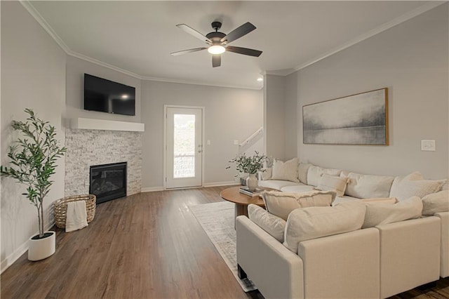 living room featuring crown molding, ceiling fan, dark wood-type flooring, and a stone fireplace